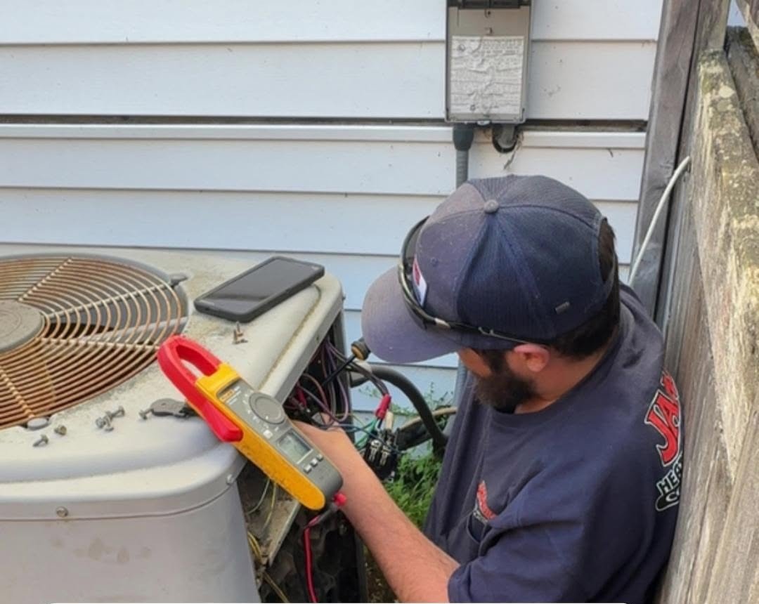 James Heating technician using a clamp meter to test electrical amperage on an outdoor AC unit during a service visit