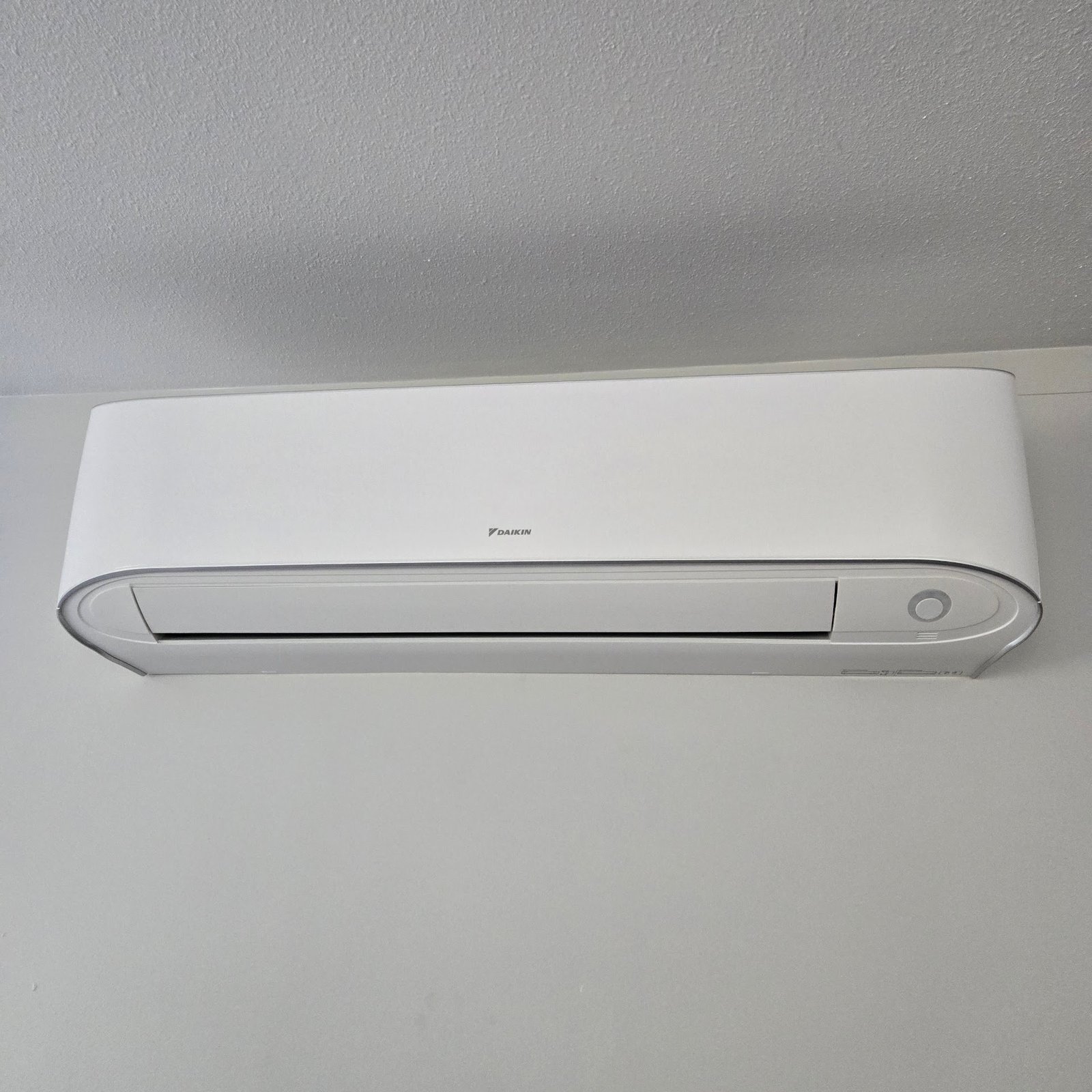 White wall-mounted ductless mini split indoor unit installed near a ceiling in a home