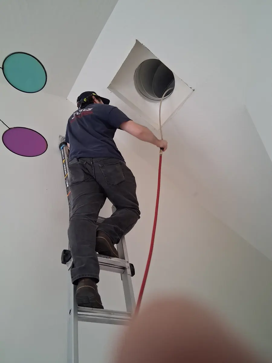 James Heating technician on a ladder cleaning a high ceiling air vent James Heating technician on a ladder cleaning a high ceiling air vent