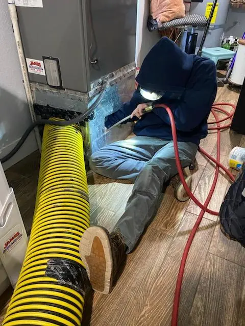 James Heating technician cleaning ductwork with a vacuum hose James Heating technician cleaning ductwork with a vacuum hose
