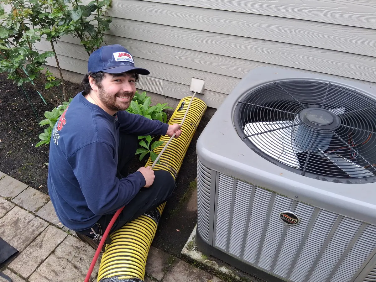 James Heating technician with a vacuum hose next to an outdoor AC unit James Heating technician with a vacuum hose next to an outdoor AC unit