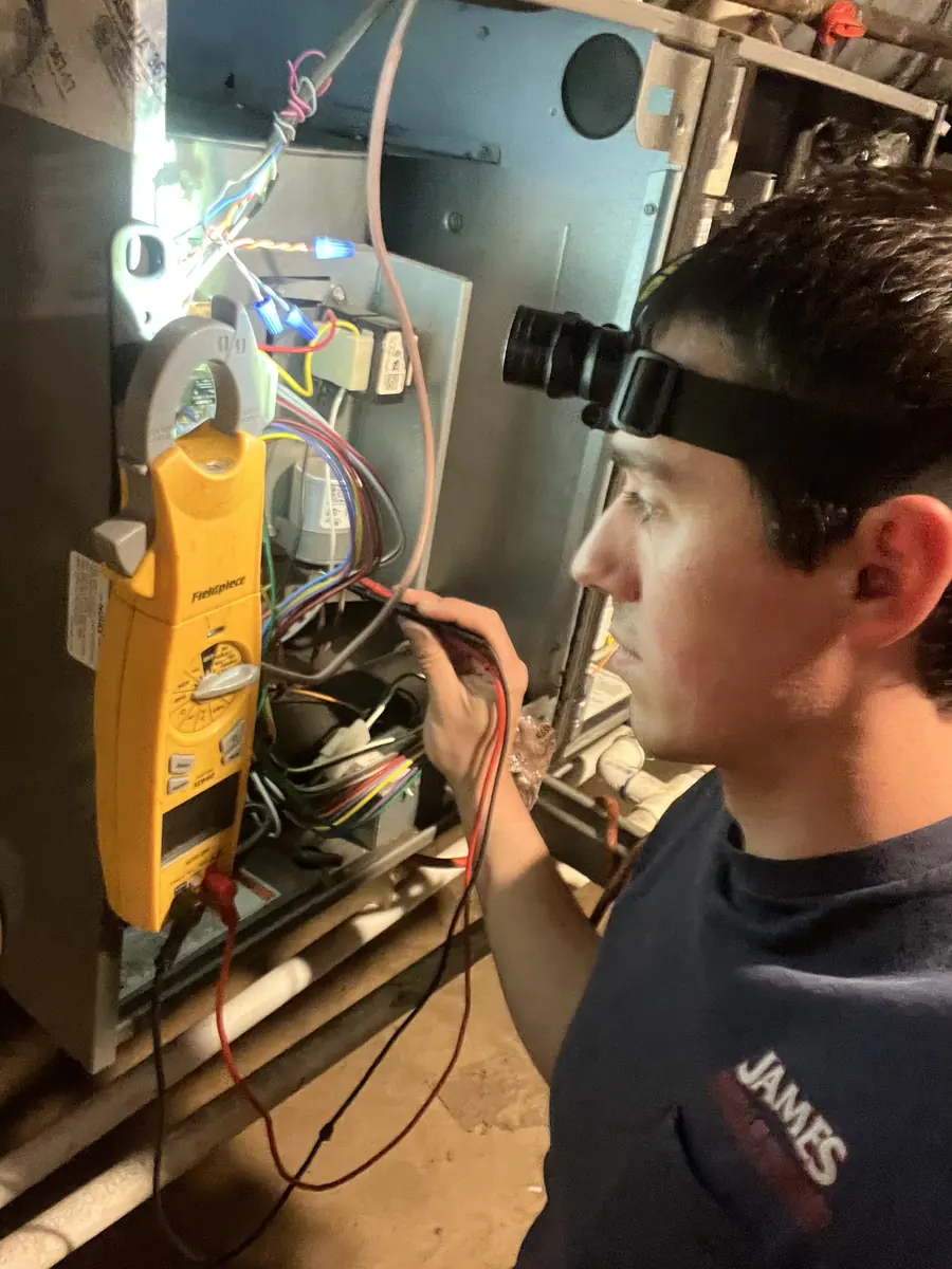 James Heating technician with a headlamp and meter diagnosing a furnace James Heating technician with a headlamp and meter diagnosing a furnace