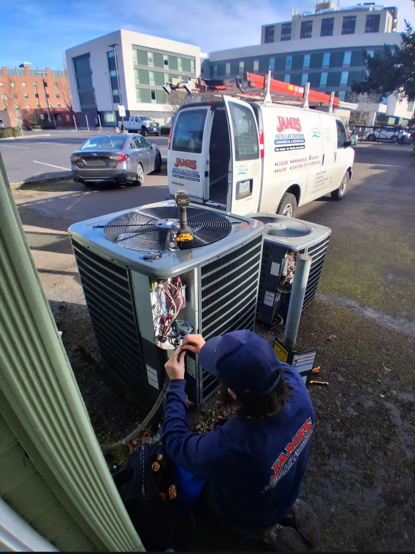 James Heating technician servicing an AC condenser beside a commercial building James Heating technician servicing an AC condenser beside a commercial building